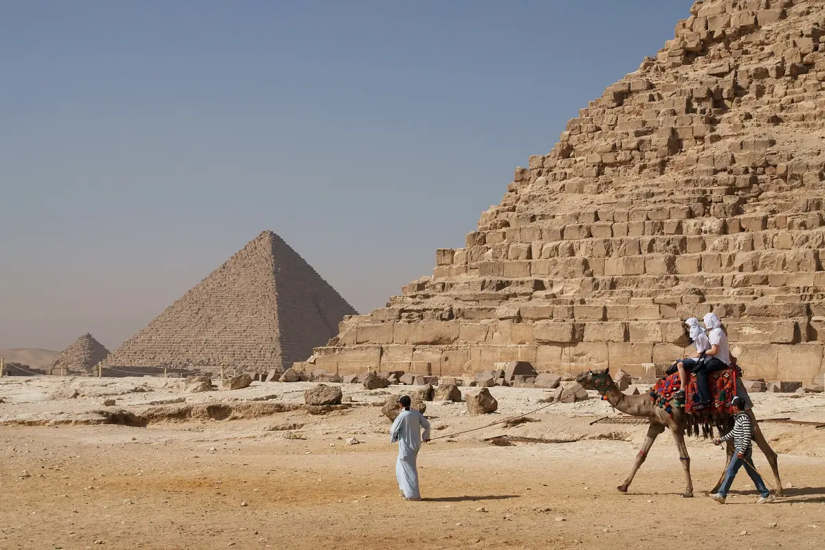 Des visiteurs à dos de chameau près des pyramides